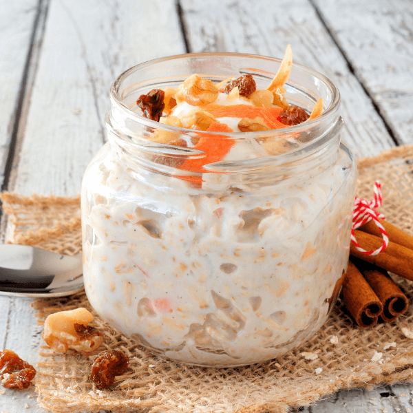 Carrot cake overnight oats with nuts and raisins in a mason jar on a rustic white wood background.