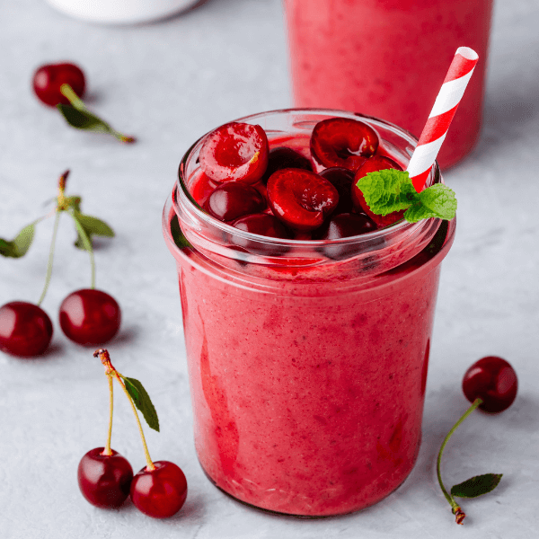 Cherry smoothie in glass jars with mint leaves and fresh berries.