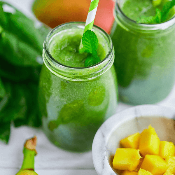 Mango with Banana and Spinach smoothie on white wooden table.