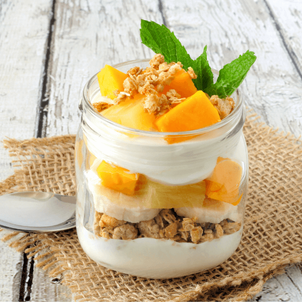 Tropical mango and pineapple parfait in a mason jar on a rustic white wood background.