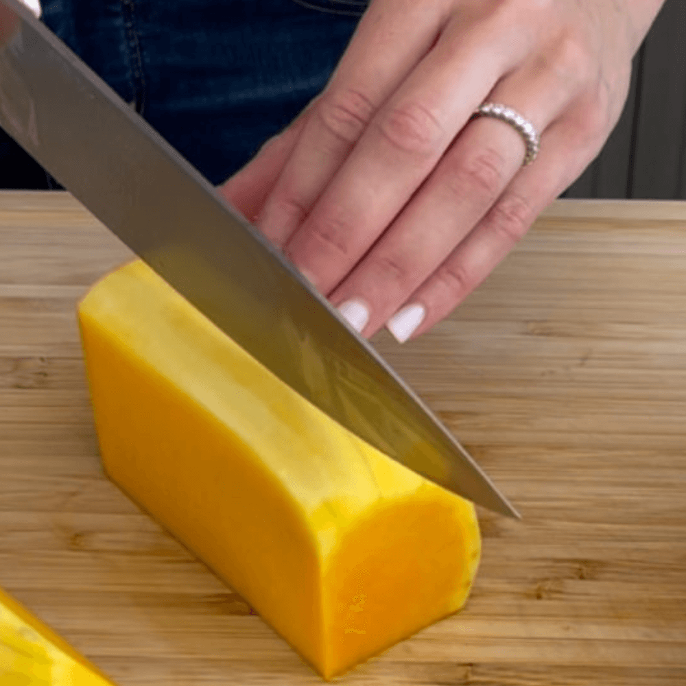 Hand slicing squash with knife on wooden cutting board.