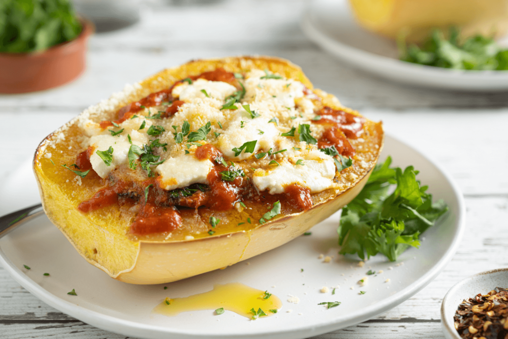 Half a roasted spaghetti squash on a plate. The spaghetti squash is baked with tomato sauce, spinach, and melted cheese.