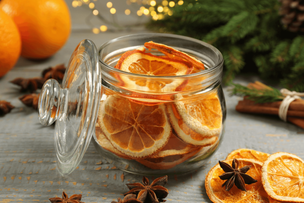 Glass jar with dry orange slices and anise stars on grey wooden table.