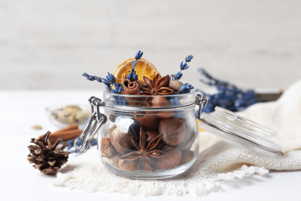 Glass flip-top jar of potpourri including dehydrated orange wheel, star anise, cinnamon sticks, and nutmeg.