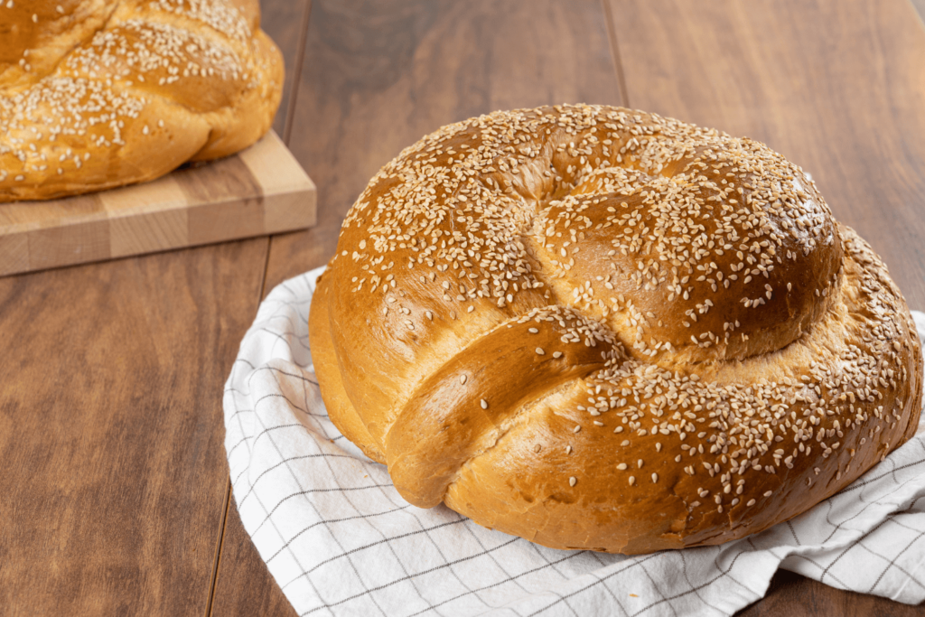 Round challah loaf on white checked dishcloth on wooden table.