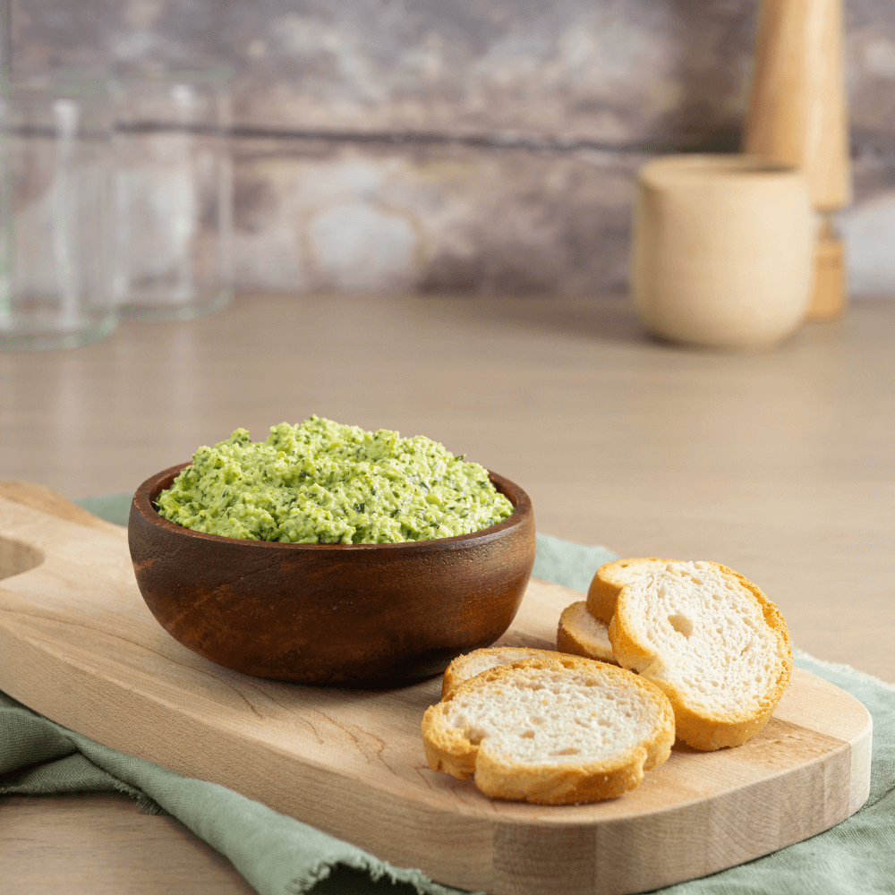 Wooden serving plank with dark wooden bowl containing Farm Boy Spicy Eda-Yummy Dip behind baguette crisps.