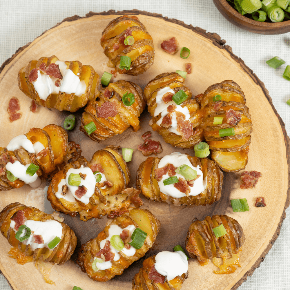 Holiday Appetizer Recipe: overhead image of log cross-section with baby hasselback poattoes garnished with cheese, bacon, sour cream, and green onions.