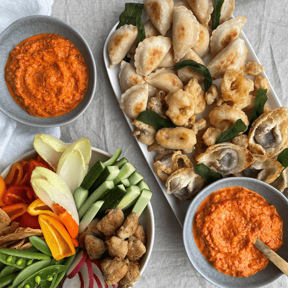 Holiday Appetizer Recipe: overhead image of two serving plates, one filled with fresh cut veggies and the other filled with crispy fried dumplings and wontons. There are two bowls of roasted red pepper dip in the upper left and lower right corners.