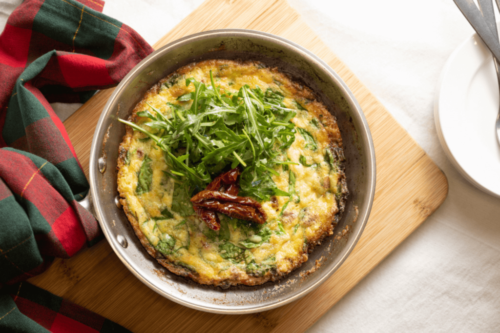 holiday leftovers: the image is shot from above and shows a skillet with a spinach frittata. The frittata is garnished with arugula and sundried tomatoes.