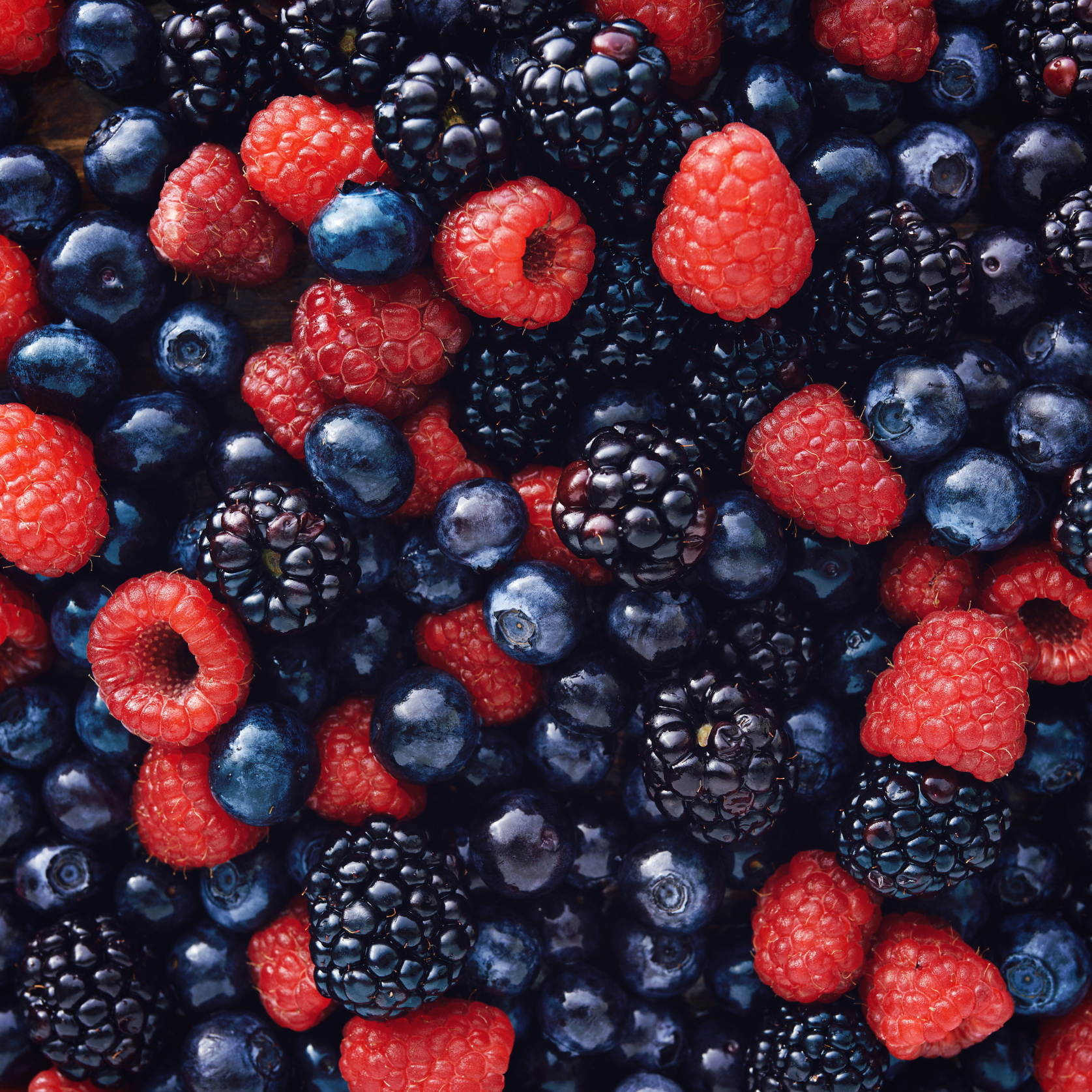 The image is shot from above and shows a mix of raspberries, blueberries, and blackberries.