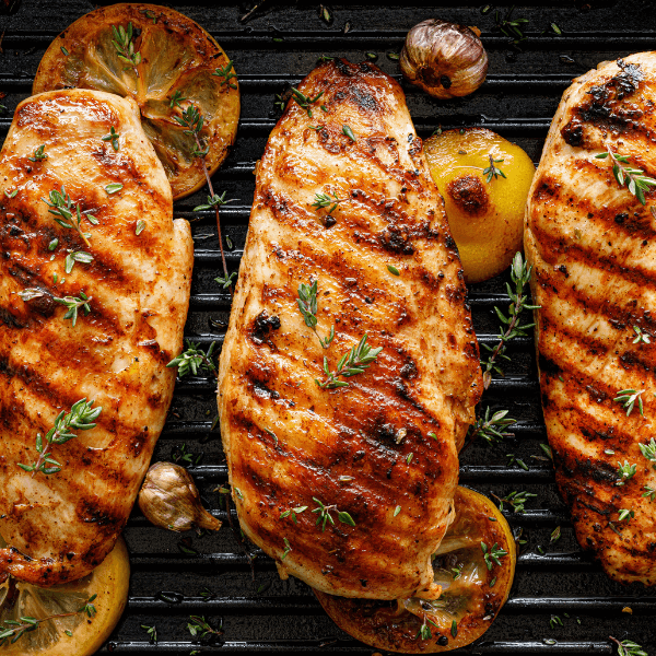 Three grilled chicken breasts with lemon on a grill.