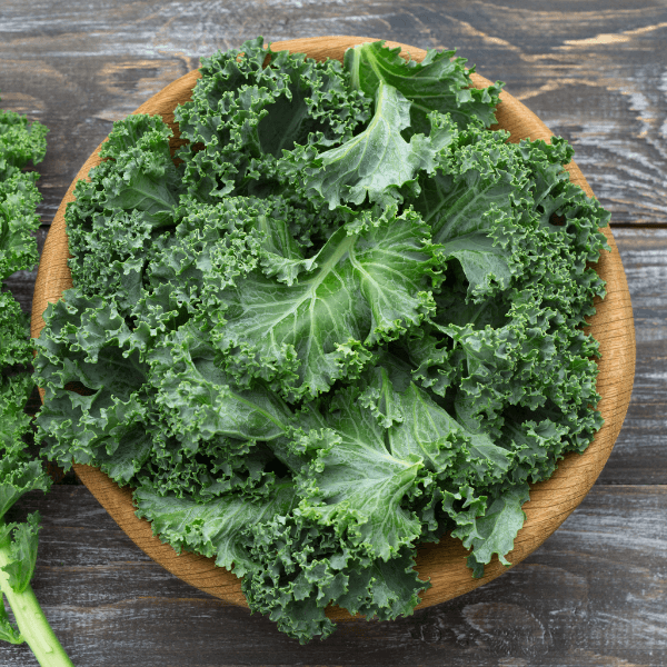 Overhead shot of fresh kale in wooden bowl on dark wood table.