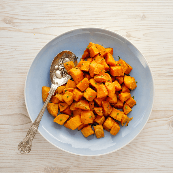 Overhead view of bowl of roasted sweet potato cubes with silver spoon.