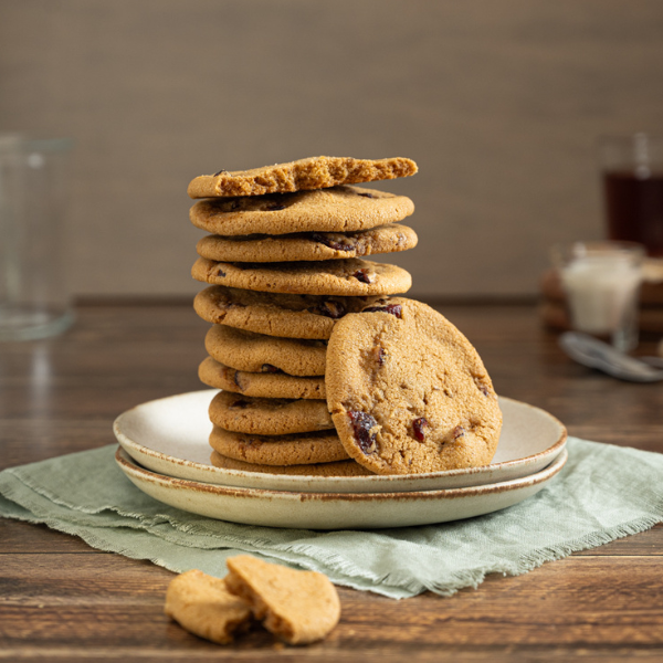 The image shows two stacked stoneware plates on a sage green raw-edge napkin. In front of the plate are two wedges of cookie. On the plate are 9.5 Lemon Cranberry Crispy Cookies. Another cookie is angled to face the camera, leaning against the stack.