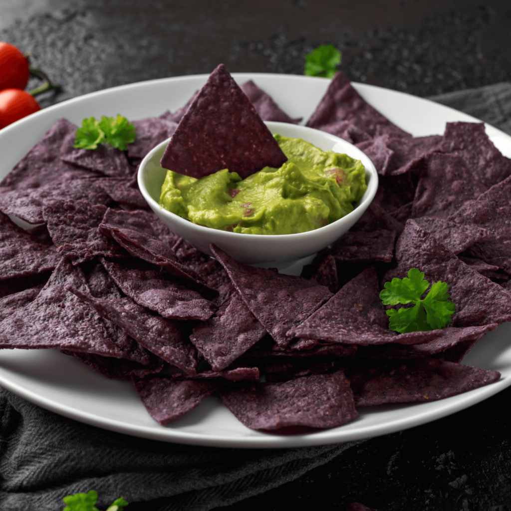 A plate of blue corn tortilla chips with a bowl of fresh guacamole in the centre.