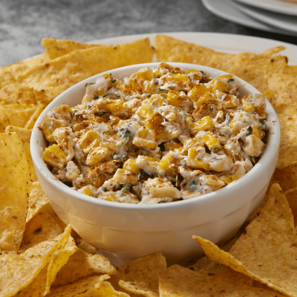 Bowl of grilled Mexican street corn dip with jalapeno peppers on a plate with tortilla chips.