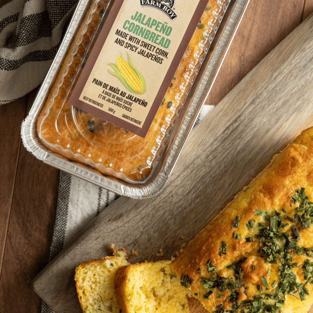 Taken from above, a packaged loaf of Farm Boy jalapeno Cornbread is visible. On a wooden cutting board, there is a sliced loaf of jalapeno cornbread.