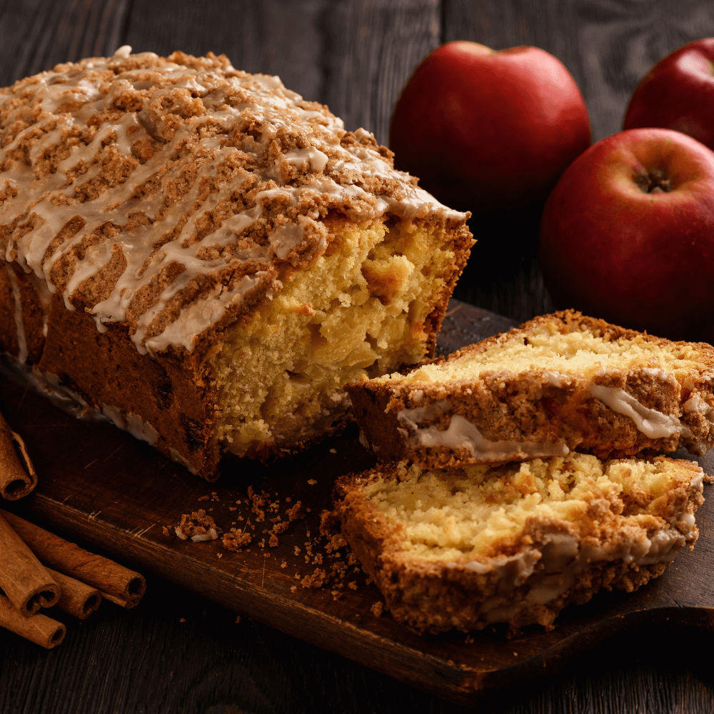 Loaf of apple bread on a wooden cutting board with two slices cut from it.