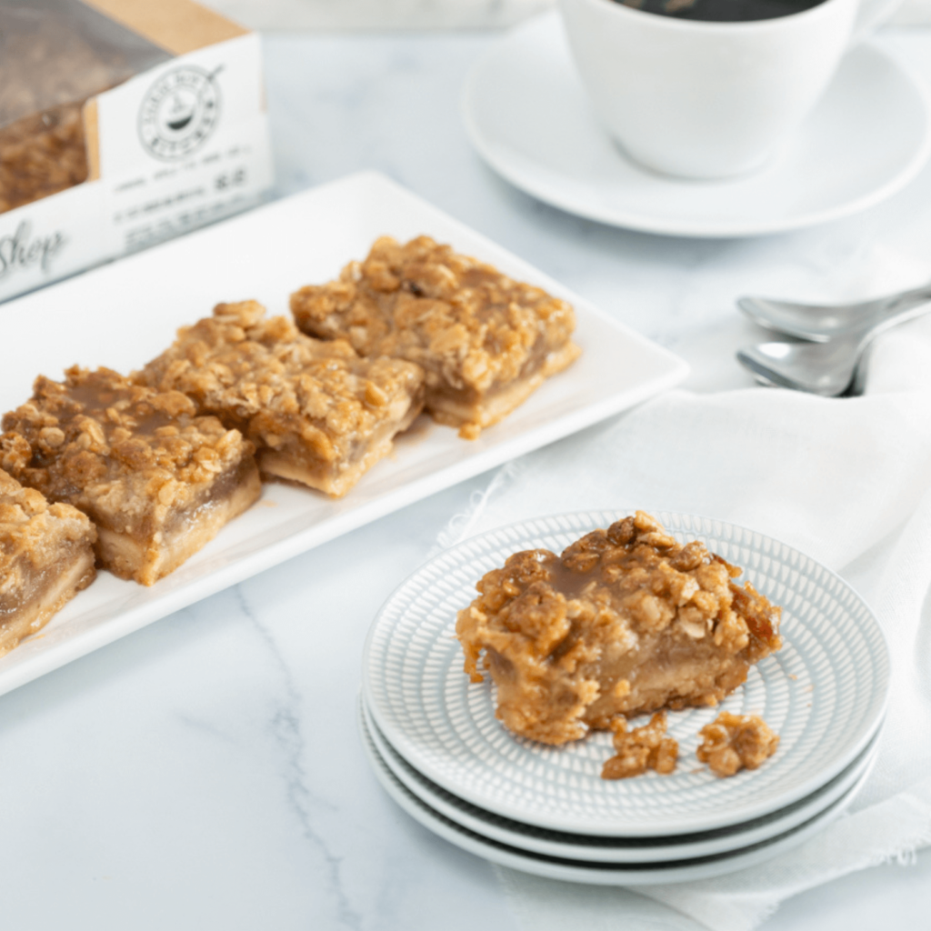 A rectangular plate bears four Salted Caramel Apple Pie Squares. A stack of three small round pale blue plates has another apple pie square.