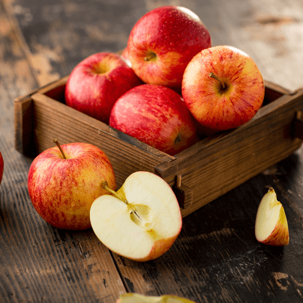 four apples in wooden box on wooden table with halved apple in front