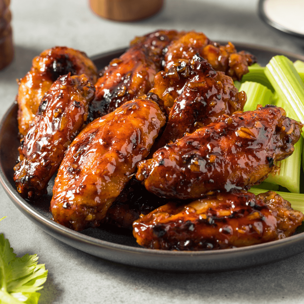 Honey garlic chicken wings on a plate with celery.