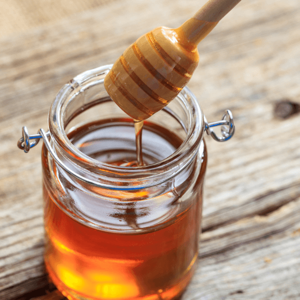 Glass jar of honey with dipper on wooden table.