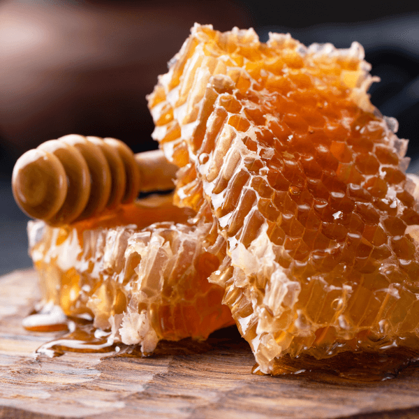 Two pieces of honeycomb with honey dipper on cutting board.