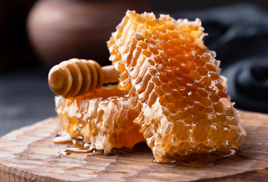 Two pieces of fresh honeycomb on wooden board with wooden honey dipper.