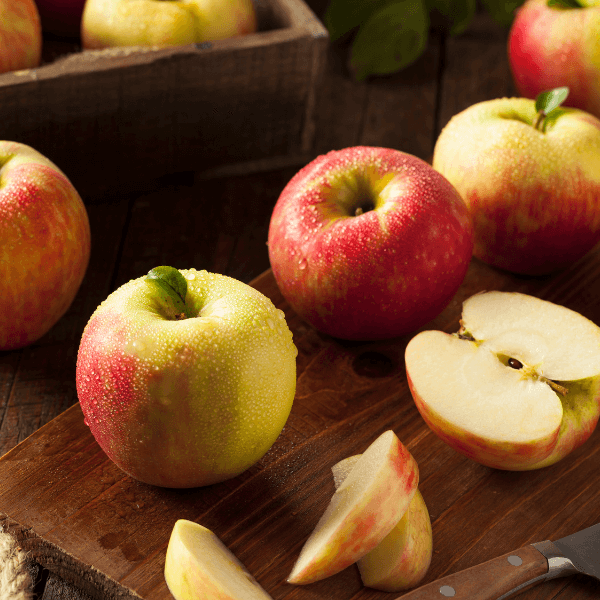 Sliced and whole honeycrisp apples on wooden cutting board.