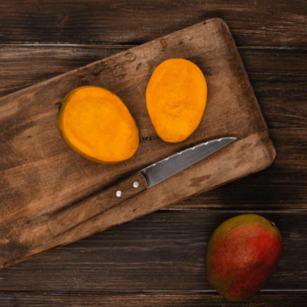 Sliced Julie mango on wooden cutting board with knife. Whole Julie mango in lower right corner.