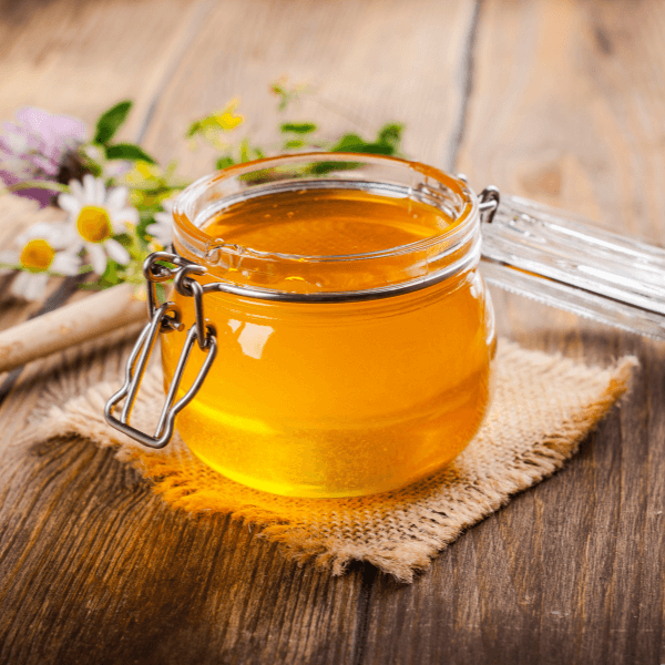 Glass jar with floral liquid honey, flowers and honey dipper.