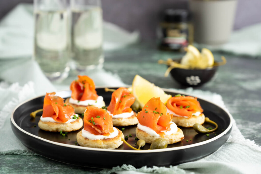 Leftovers Recipe: The image shows a black plate upon which are six potato cakes made with leftover mashed potatoes and finished with sour cream and smoked salmon.