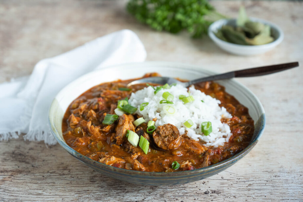 Leftovers Recipe: The image shows a bowl of turkey and sausage gumbo made with leftover holiday turkey. It is served with a side of rice and garnished with sliced green onions.