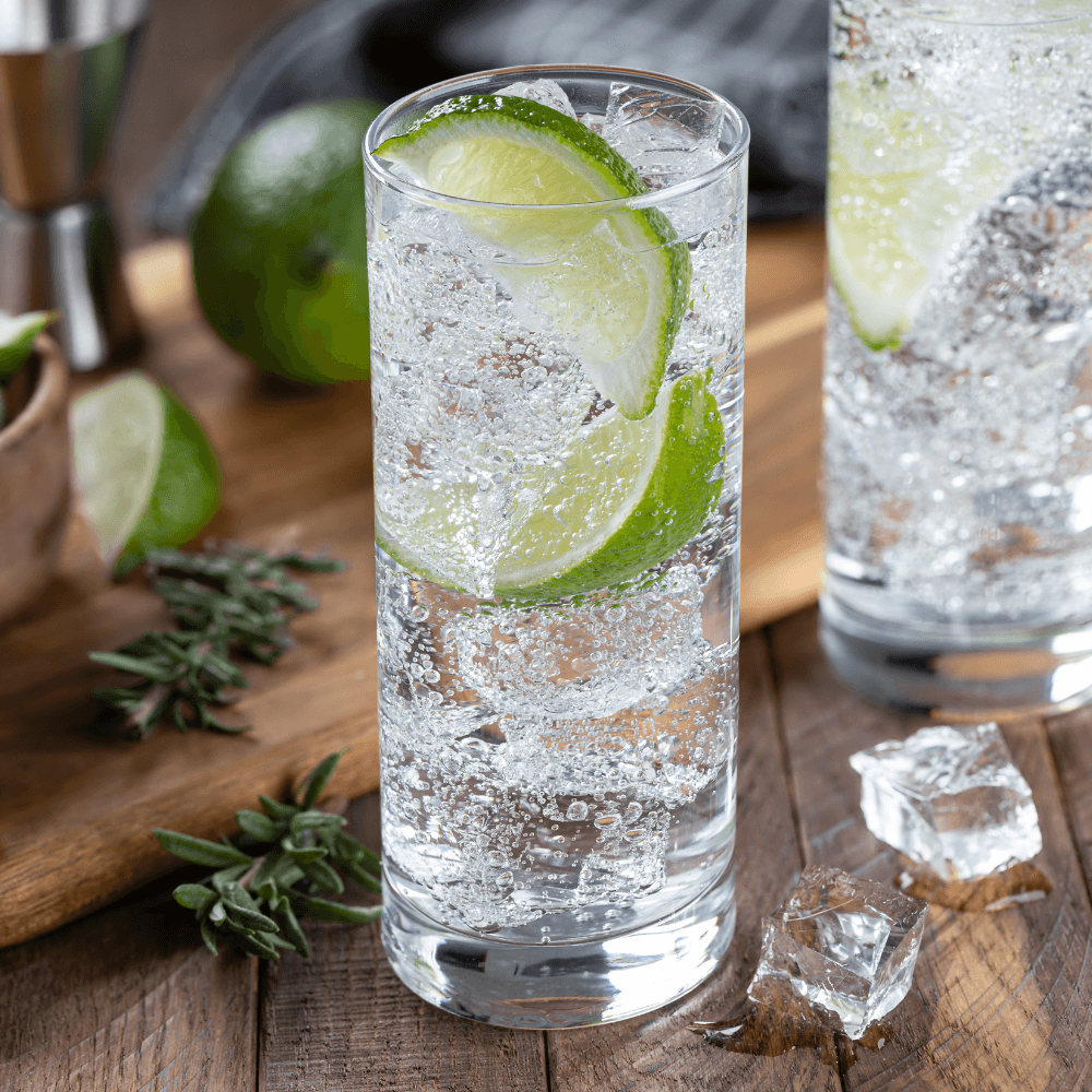 Stock image of tall glass filled with ice and carbonated water garnished with two lime wedges on rustic wooden table.