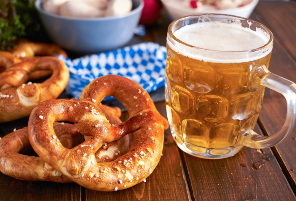 Traditional Munich pretzel next to mug of beer on wooden table for Oktoberfest. Close up.