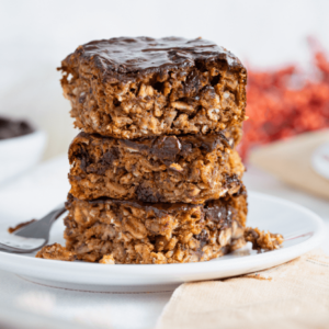 The image shows a white plate with a stack of three pumpkin pecan and chocolate protein bars stacked on top of one another.