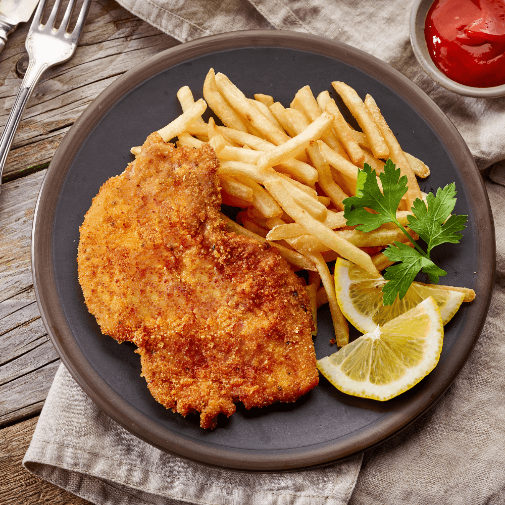 Stock image of pan-fried pork schnitzel on a plate with fries and two lemon slices.