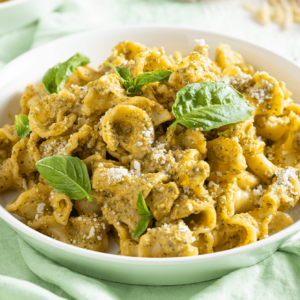 A white bowl filled with Artisan Riccioli Pasta tossed in a green pesto sauce, topped with grated Parmesan cheese and fresh basil leaves.