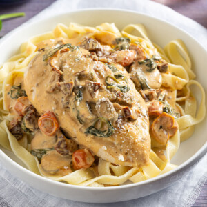 Creamy Tuscan Chicken with Tomatoes, Mushrooms and Spinach in a bowl over pasta.