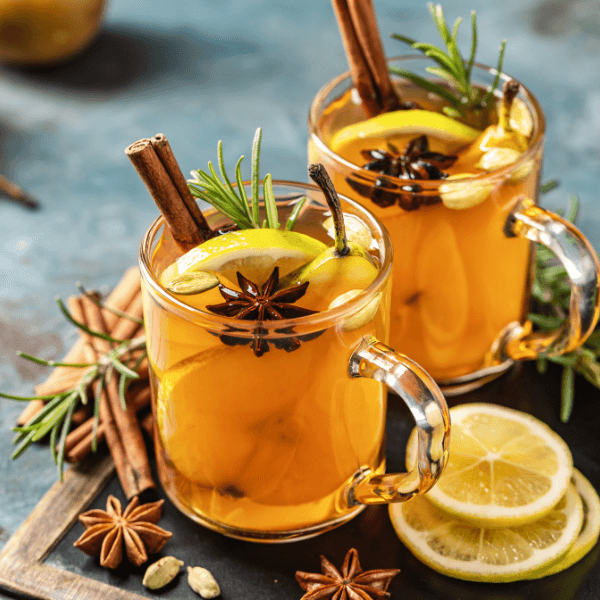 Hot drink cocktail for New Year, Christmas, winter or autumn holidays. Toddy. Mulled pear cider or spiced tea or grog with lemon, pear, cinnamon, anise, cardamom, rosemary.