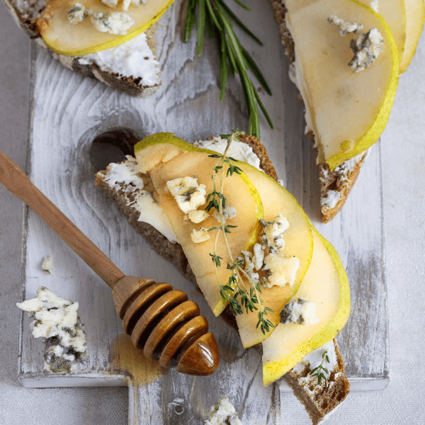 Toast or bruschetta with ricotta or cream cheese, pear, honey and blue cheese on white wooden cutting board.