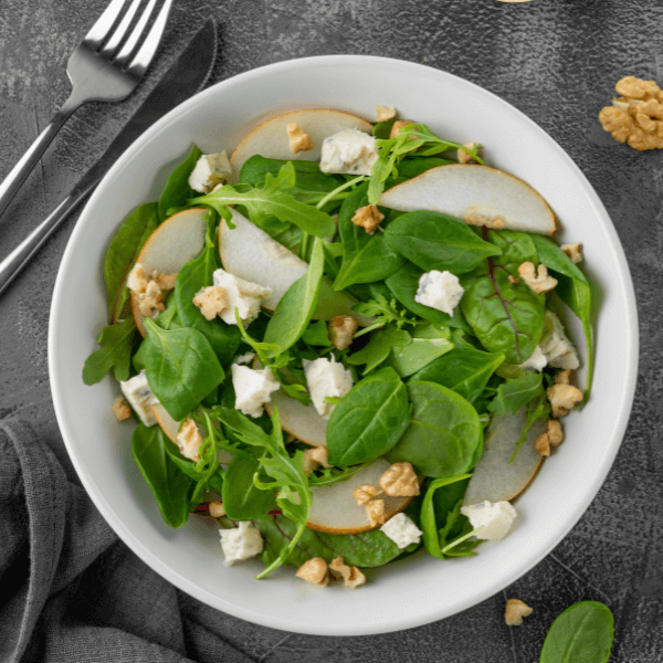 Salad with spinach, arugula, fresh pear, nuts and gorgonzola cheese with olive oil in a bowl.